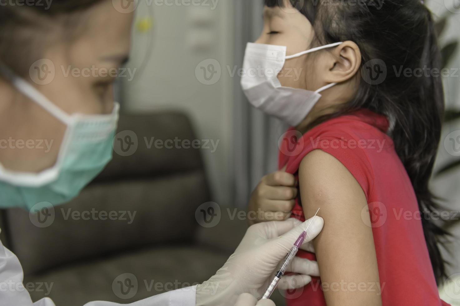 Asian doctor injection vaccine for protecting virus covid-19 to a girl wear medical mask,People are Girls are vaccinated against influenza every year. photo