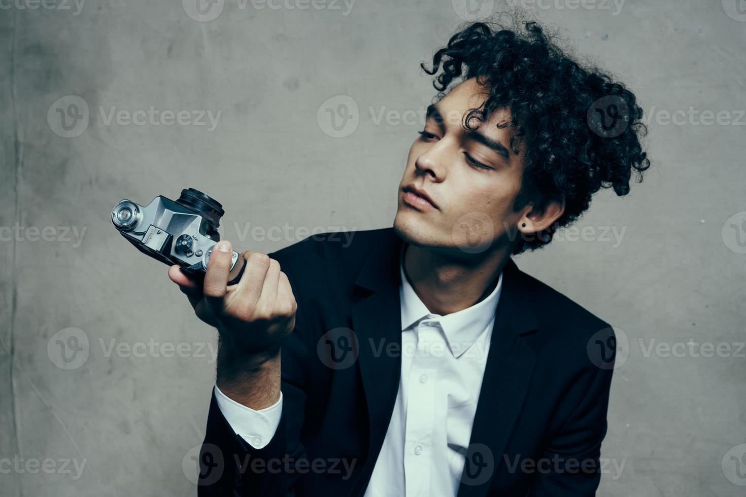 curly-haired man in a classic suit looks at the camera in his hand studio hobby photo