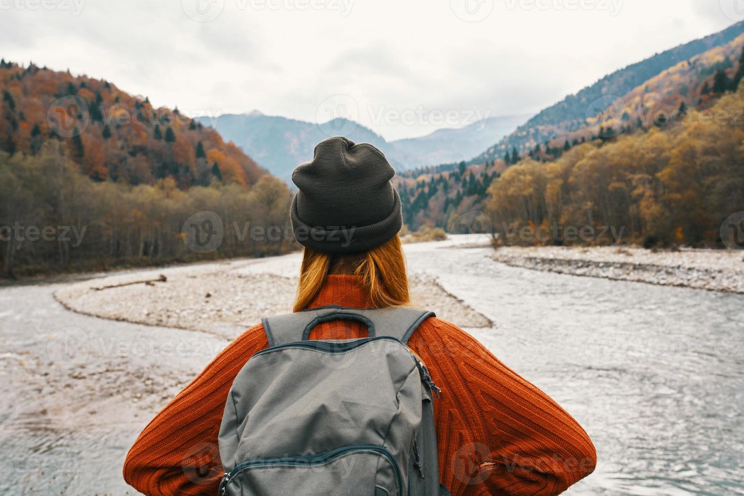 woman in a sweater and cap with a backpack on her back in the mountains on nature landscape photo