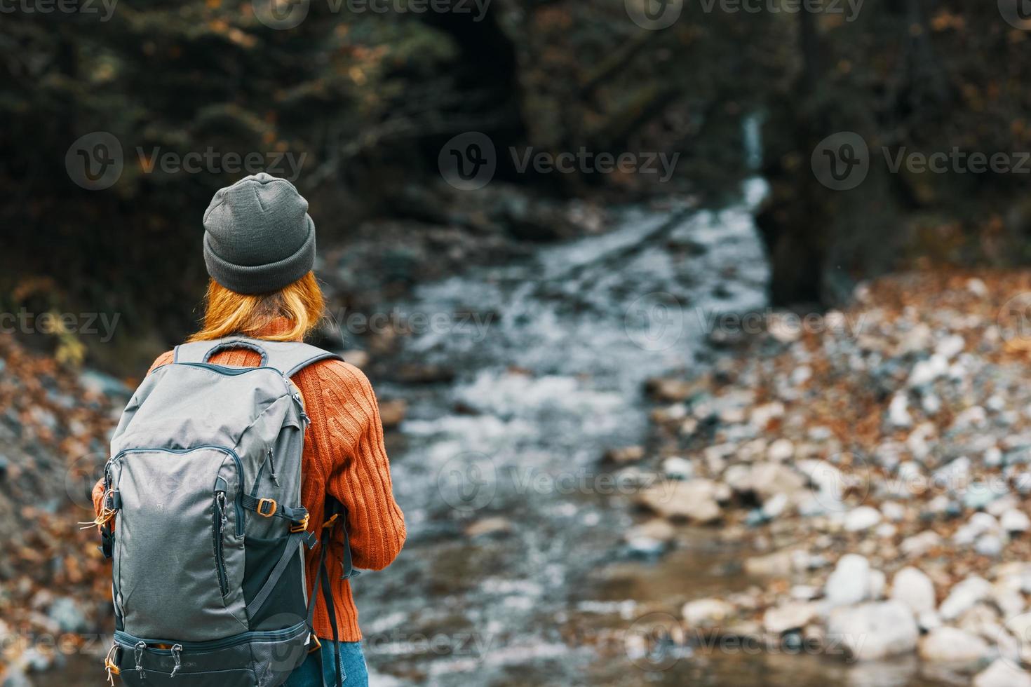 woman near the river in the mountains with a backpack on her shoulders are resting in the autumn forest photo