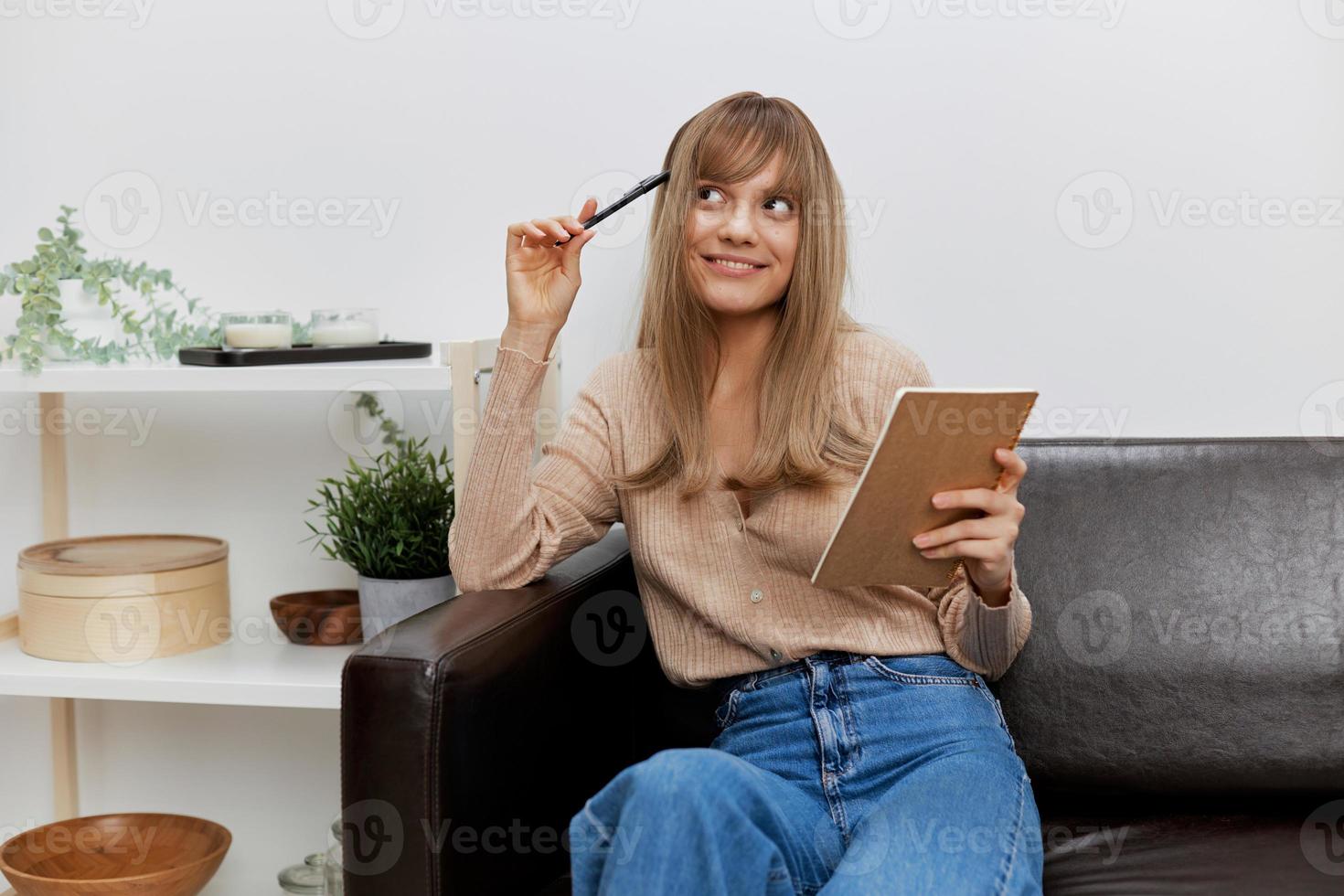 Pensive dreaming happy blonde student lady with copybook looks up thinks about future plans sitting in sofa couch. Female client have shrink appointment in psychological help office. Copy space photo