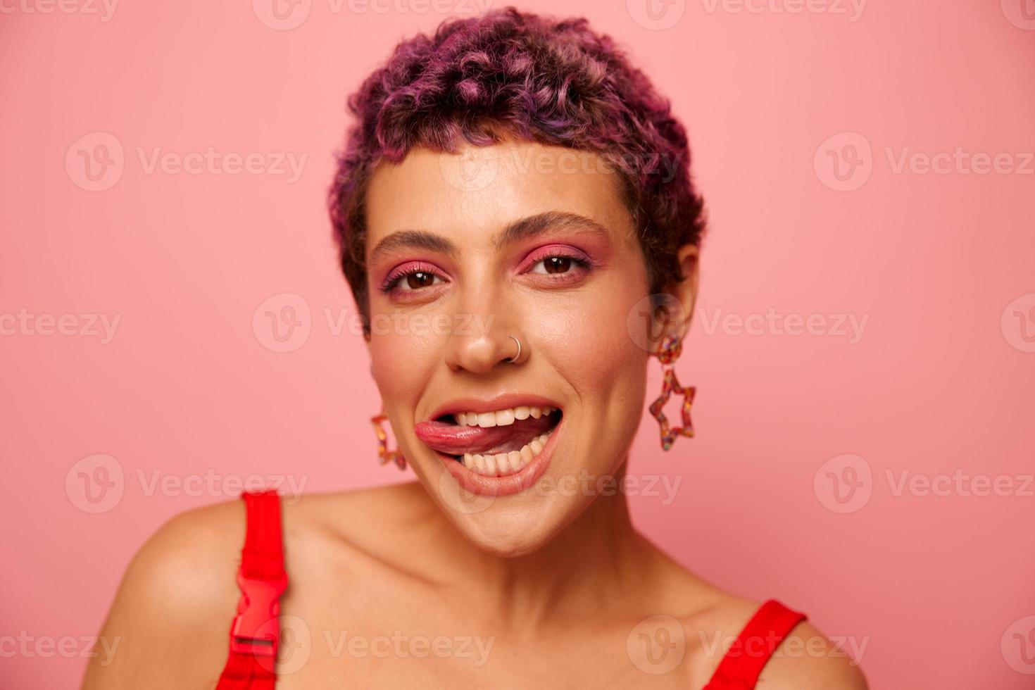 Fashion portrait of a woman with a short haircut of purple color and a smile with teeth in a red top on a pink background happiness photo