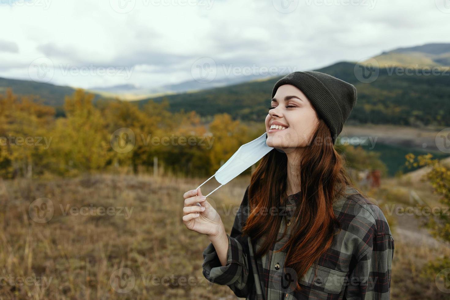 Modern woman in a medical mask smiles outdoors in the mountains in the forest photo