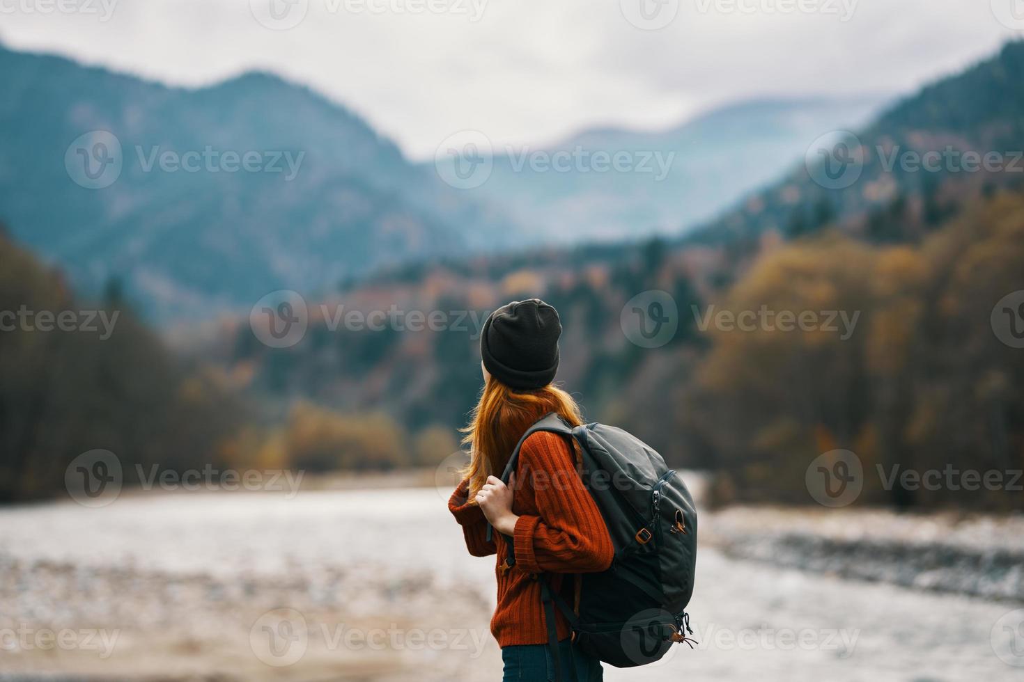 woman in a hat with a backpack are resting in the mountains in nature near the river photo