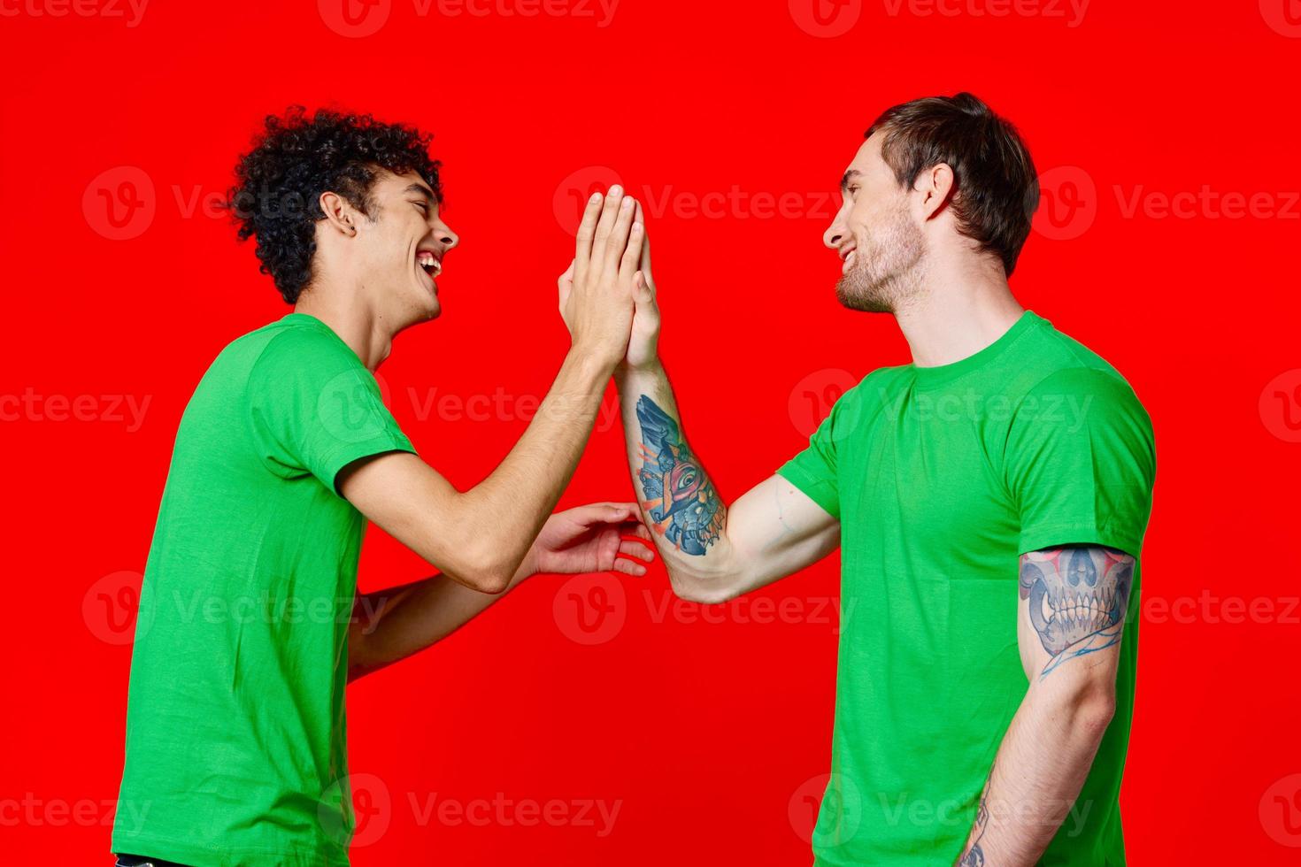 two friends in green t-shirts communication red background studio photo