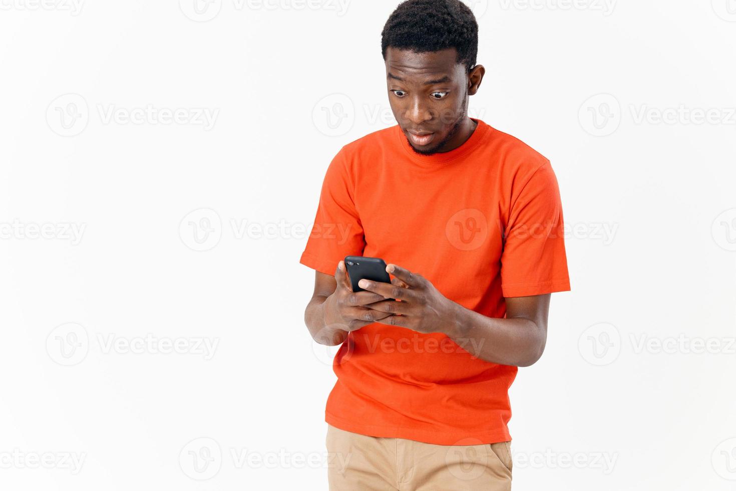 a guy in an orange t-shirt looks at the screen of a mobile phone photo