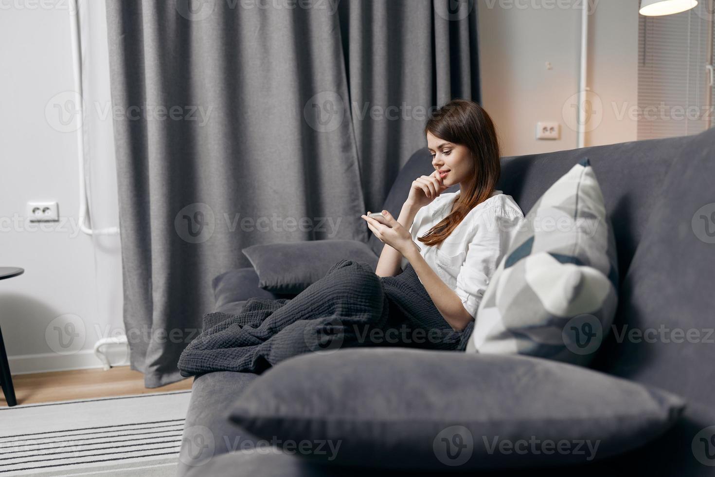 woman covered with a blanket sits on the couch with a mobile phone in her hand side view photo