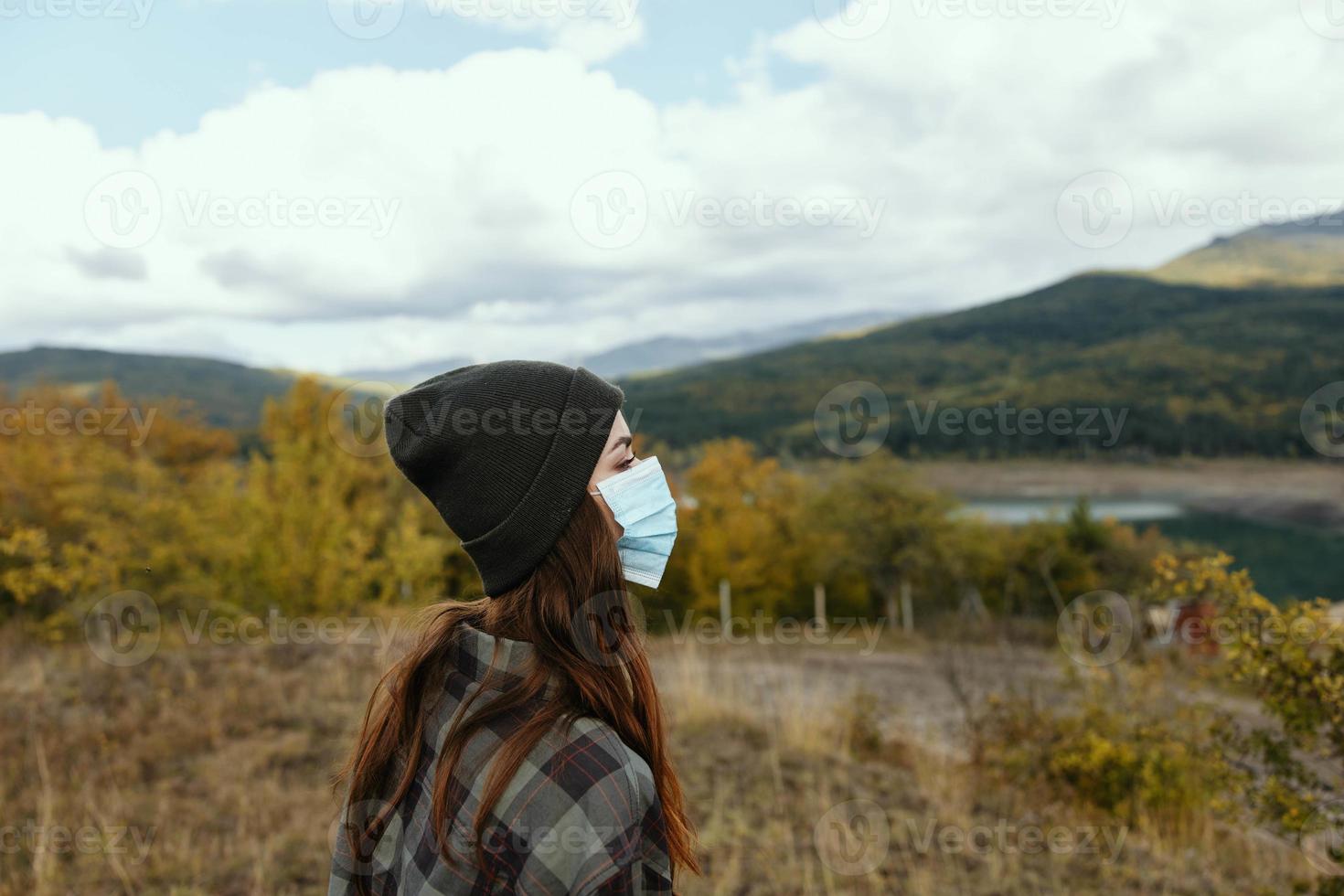 Woman in warm caps in the autumn forest with a medical mask on her face photo