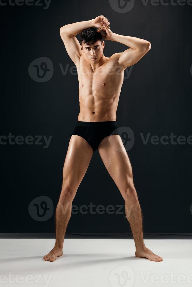 handsome man with muscular naked body in black panties posing against dark background photo