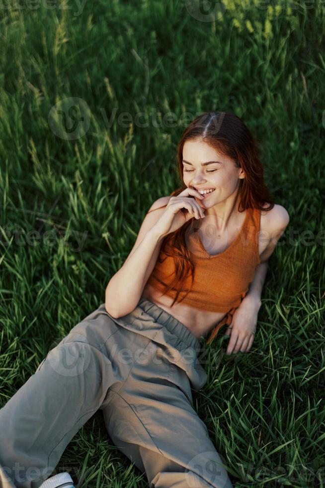 View from above a woman lying on the grass smiling and looking into the cameras happy lifestyle in the park on the green grass in the sunset light photo