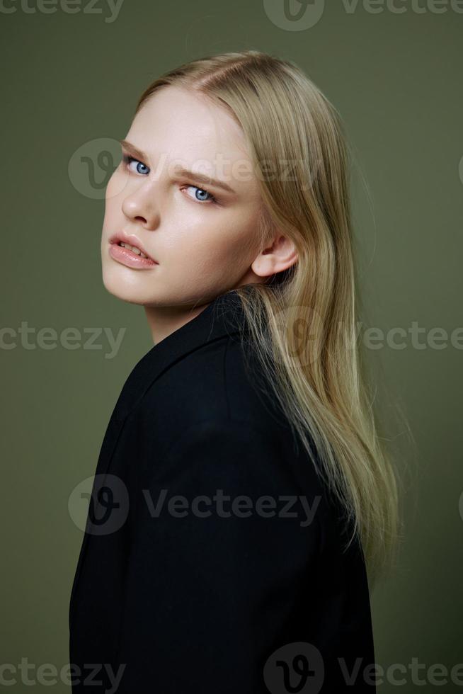 A beautiful girl looks half-turned into the camera at you posing on a green background in a jacket in the studio photo