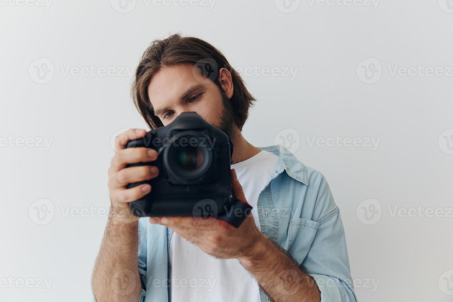 Man hipster photographer in a studio against a white background holding a professional camera and setting it up before shooting. Lifestyle work as a freelance photographer photo