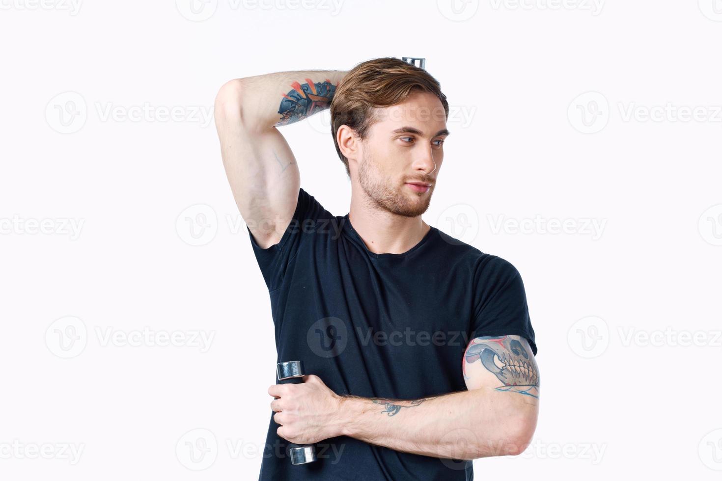 guy with dumbbells holds his hand behind his head and light background black t-shirt sport fitness photo