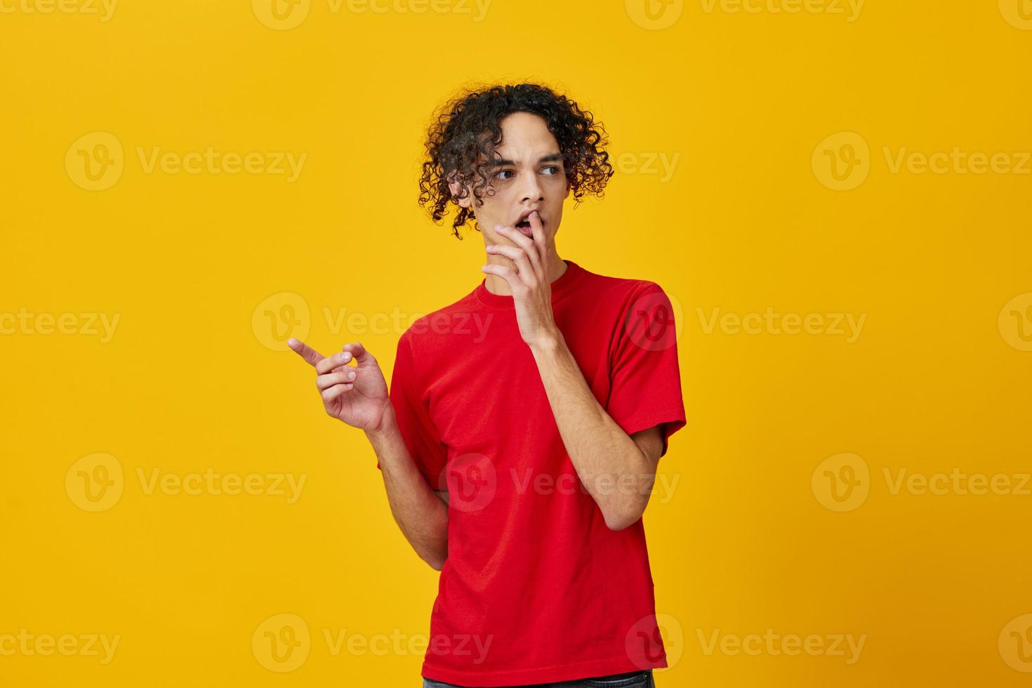 Shocked funny Caucasian young man in red t-shirt point finger aside posing isolated on over yellow studio background. The best offer with free place for advertising. Emotions for everyday concept photo