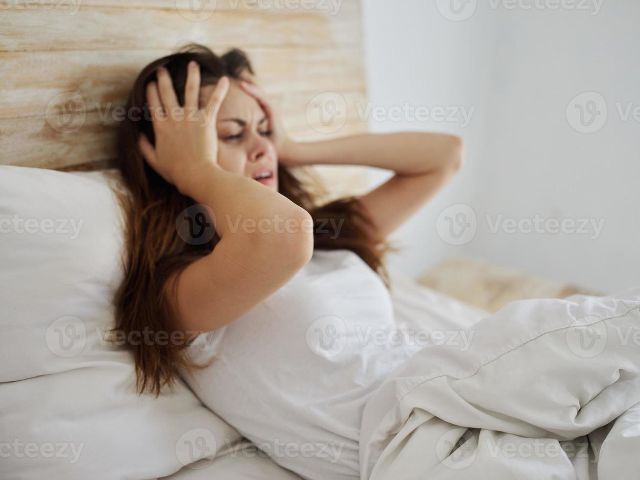 crying woman holding her head health problems lying in bed photo