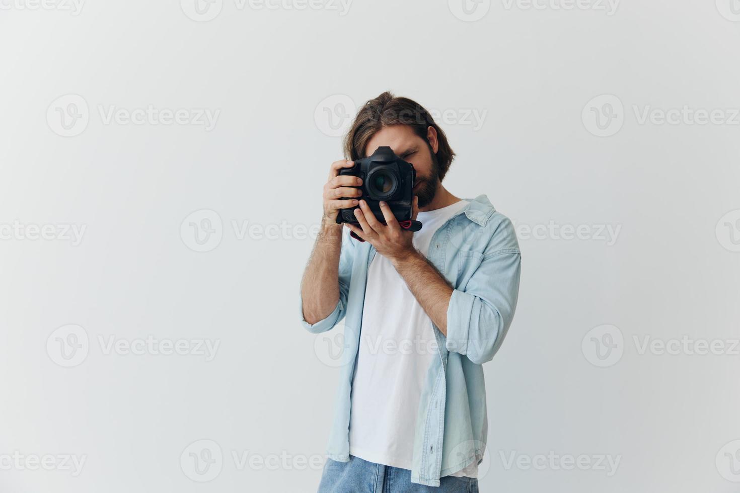 A male hipster photographer in a studio against a white background looks through the camera viewfinder and shoots shots with natural light from the window. Lifestyle work as a freelance photographer photo