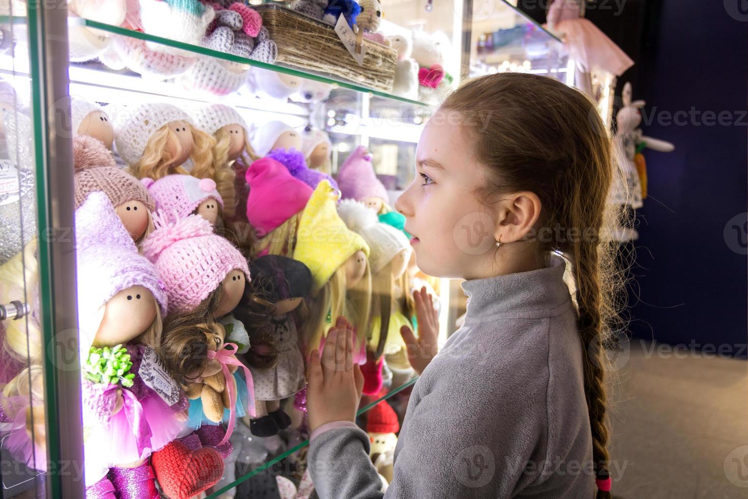 little cute girl looks with admiration at handmade dolls in a shop window photo
