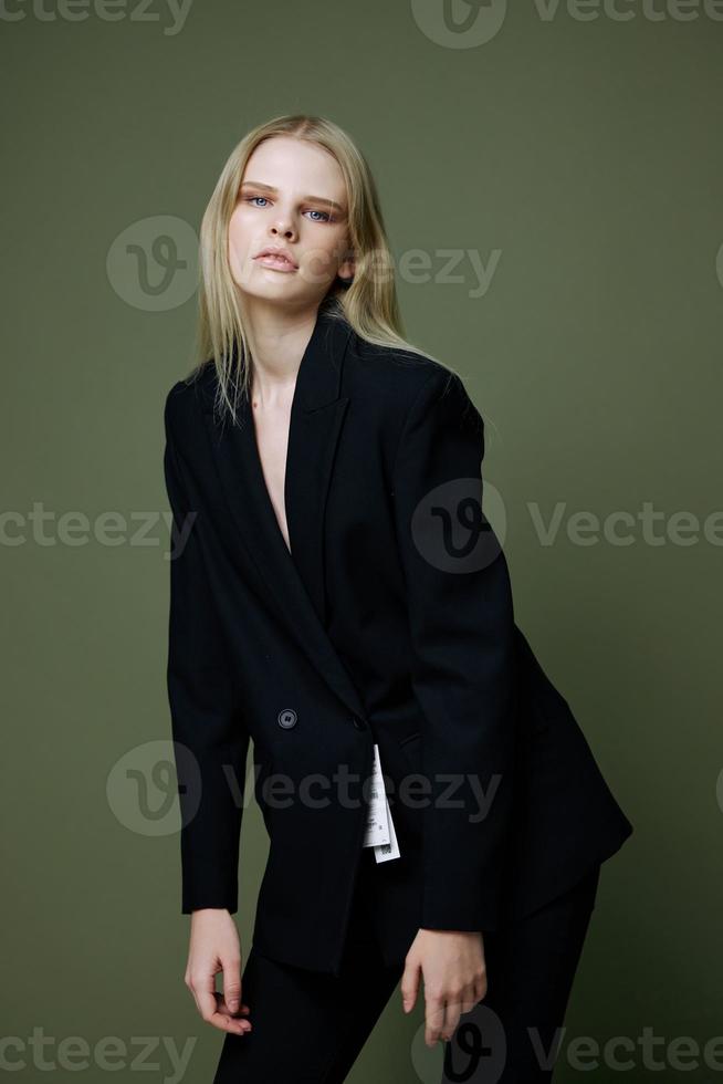 A stunning elegant girl in a black suit leans forward and poses professionally on a green background in the studio. The concept of advertising for designer brands photo