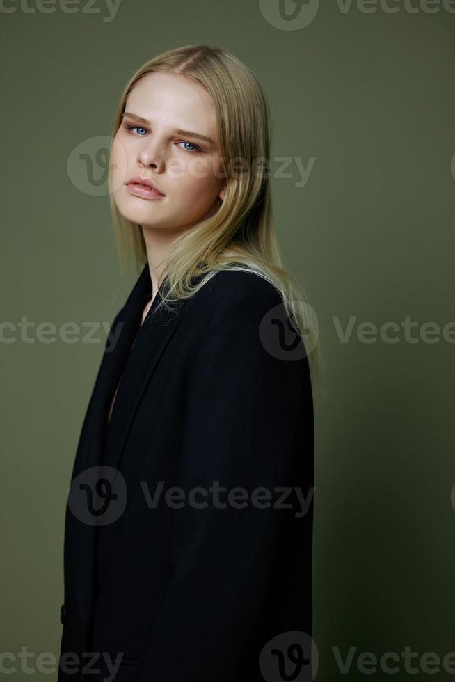 rubia mira terminado su hombro en un negro chaqueta posando medio vuelto en el estudio en un verde antecedentes. el concepto de elegante Moda fotografía foto