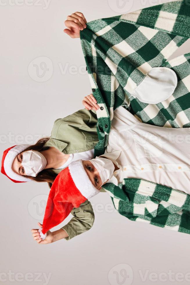 Happy men and women in New Year's hats and in a medical mask on a beige background photo