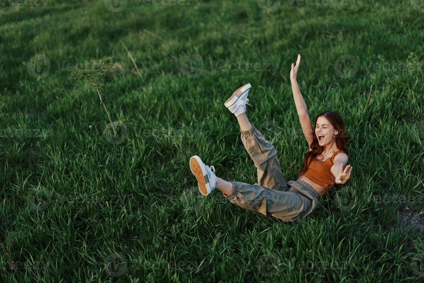 A young woman is playing in the park with us in the grass and falls to the ground smiling happily in the sunlight. Resting in nature, harmony with the body photo
