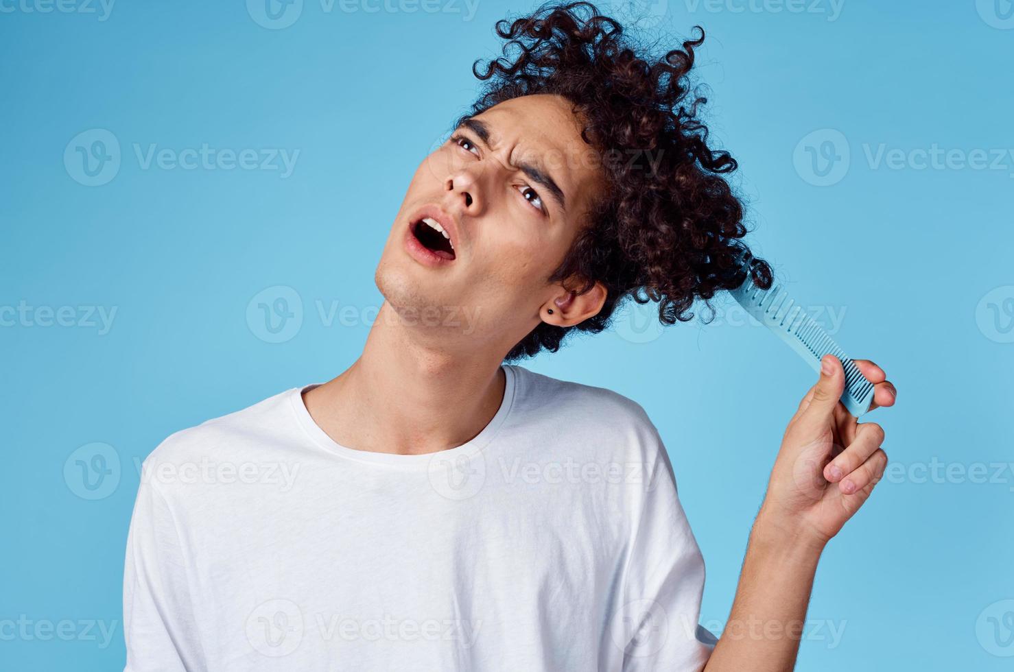 curly guy in a white t-shirt comb emotions blue background photo