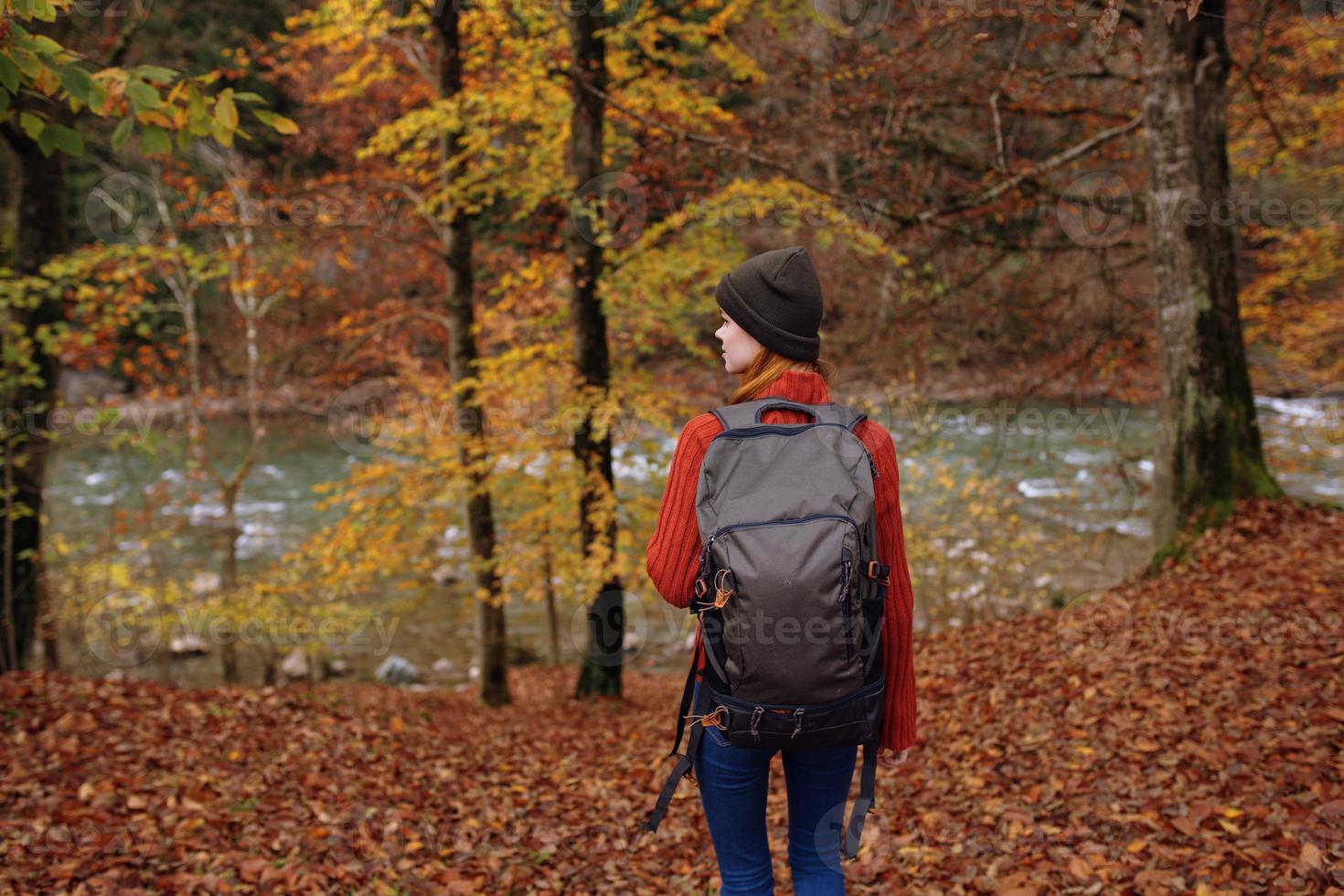 woman in the park in autumn near the river and a backpack on her back back view photo