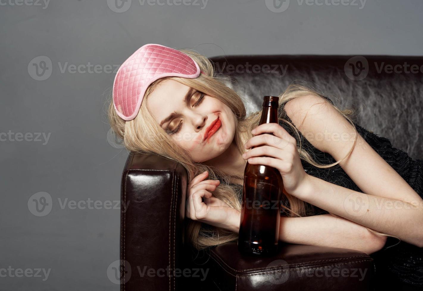 A woman with a pink mask on her head and a bottle of beer sleeps on the couch photo