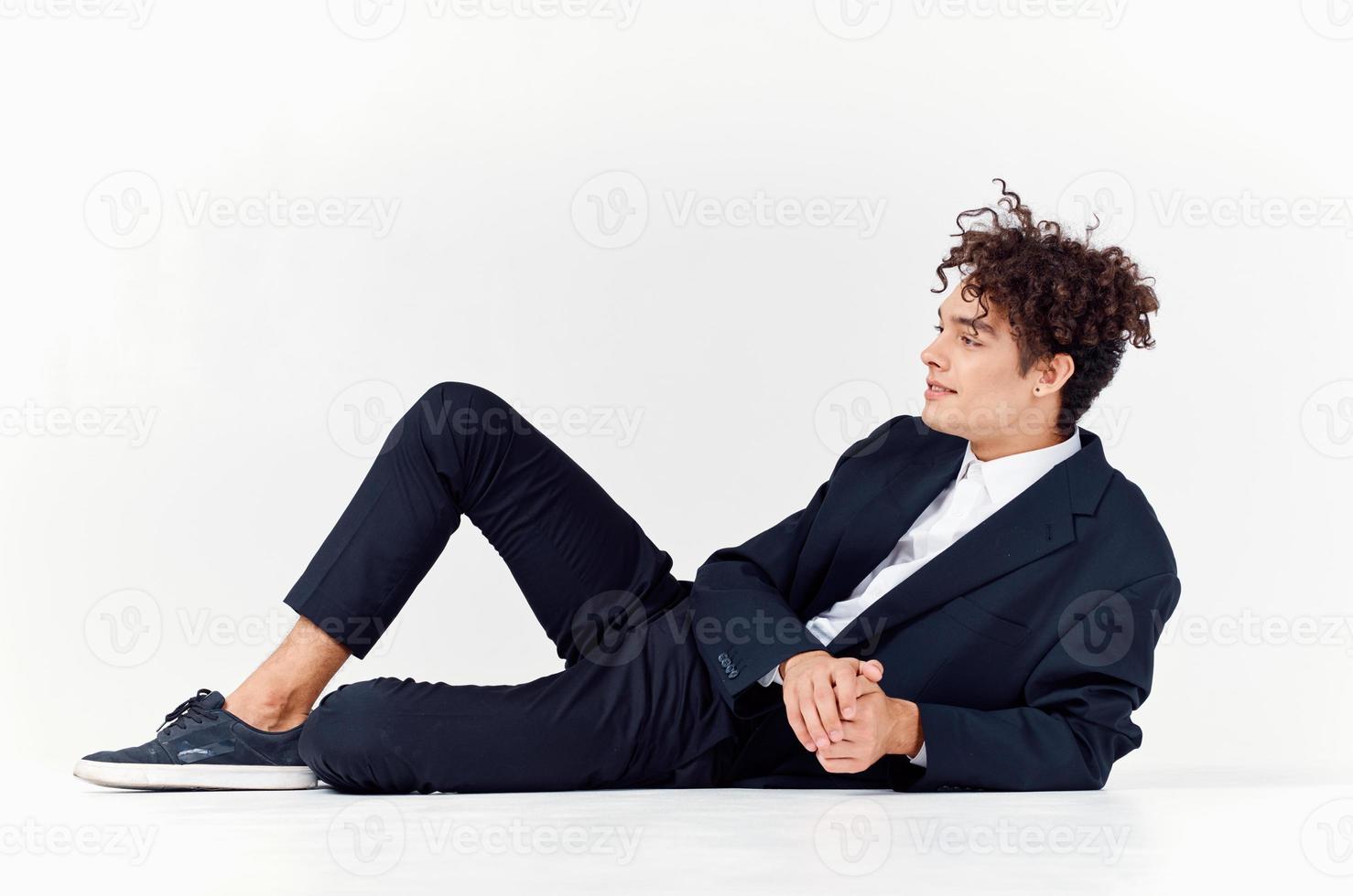 a fashionable guy in trousers and a jacket lies on the floor In a bright room, curly hair sneakers photo