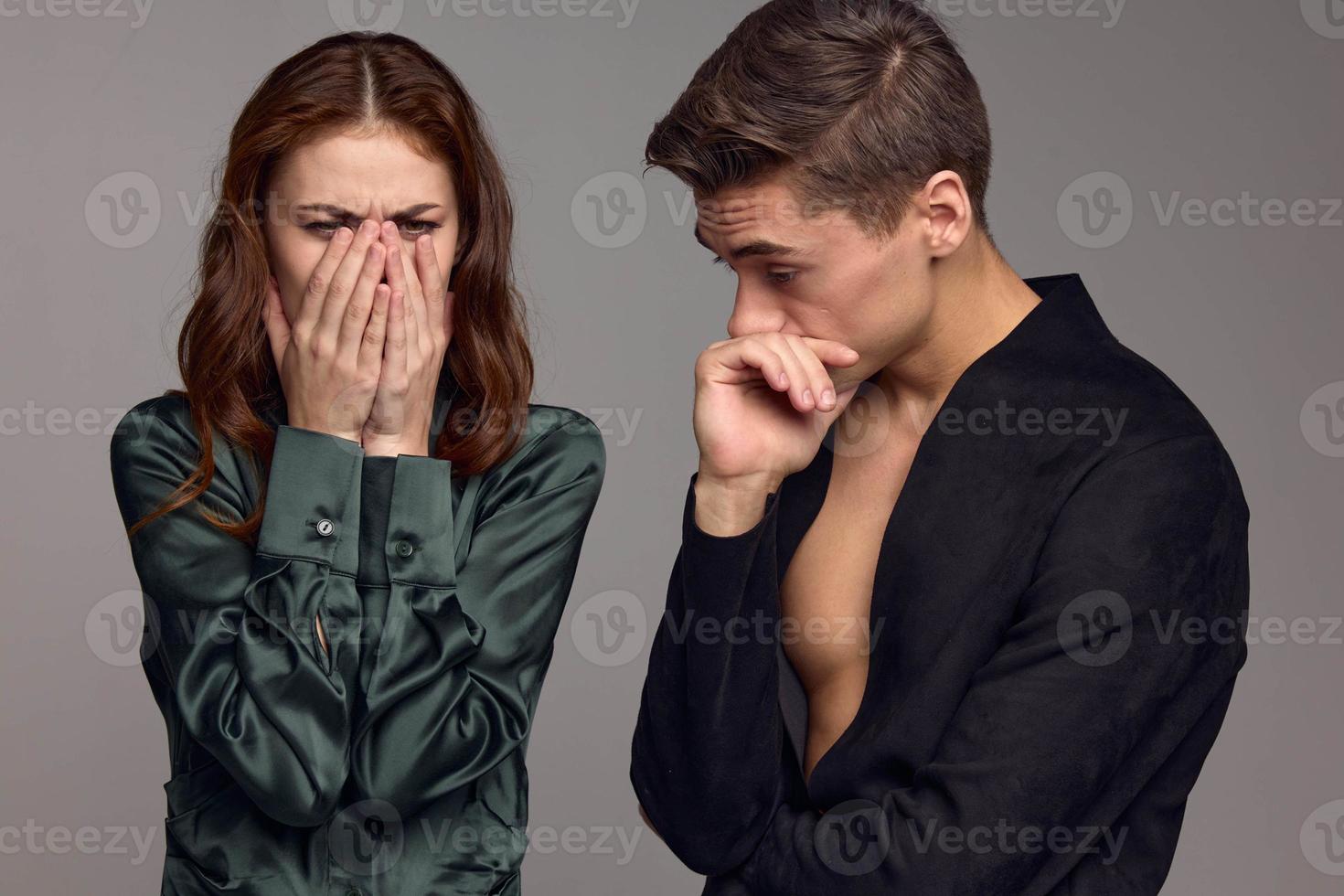 A puzzled man and an upset woman on a gray background are gesturing with their hands photo