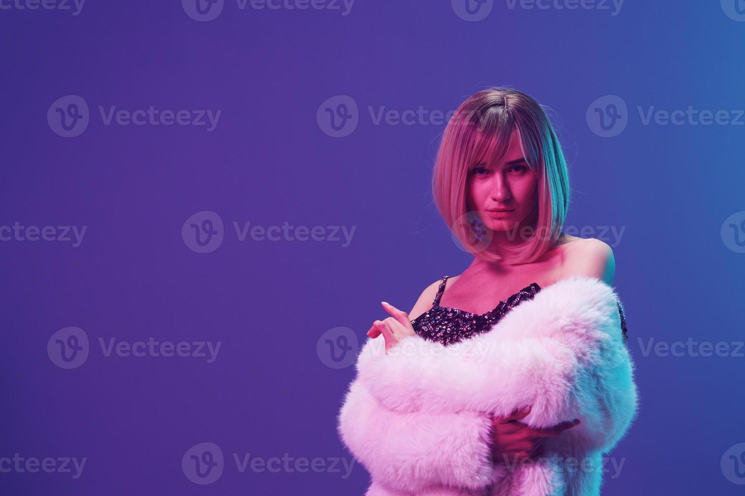 Sexy adorable blonde woman in fluffy fur coat sparkly dress with open shoulders posing isolated in blue violet pink color light studio background. Neon party Fashion concept. Copy space Banner photo