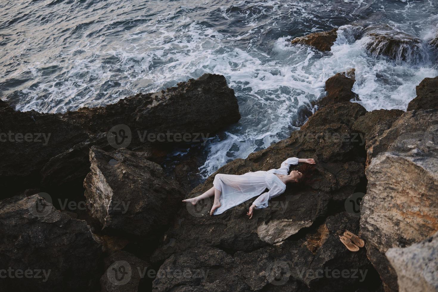 descalzo mujer acostado en rocoso costa con grietas en rocoso superficie paisaje foto