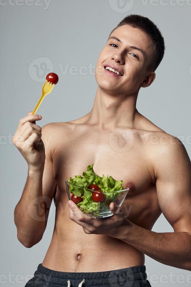 Cheerful sporty guy with a naked torso plate with salad healthy food photo