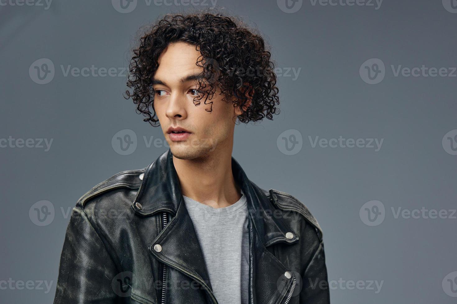 Pensive handsome stylish tanned curly man leather jacket looks aside posing isolated on over gray studio background. Cool fashion offer. Huge Seasonal Sale New Collection concept. Copy space for ad photo