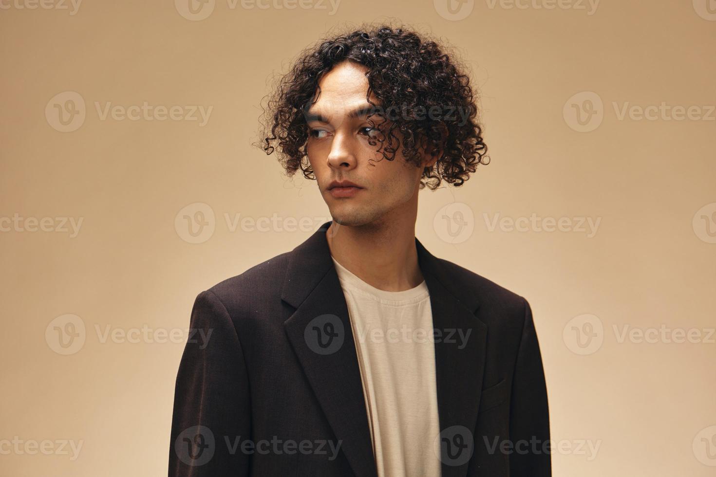 Serious stylish awesome tanned curly man in classic brown jacket posing isolated on over beige pastel background. Fashion New Collection offer. Retro style concept. Free place for ad photo