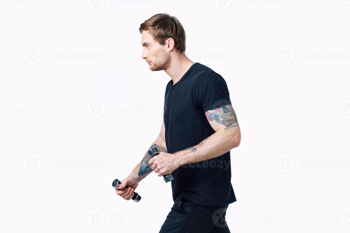 nice guy with dumbbells in a black t-shirt and trousers goes in for sports side view photo