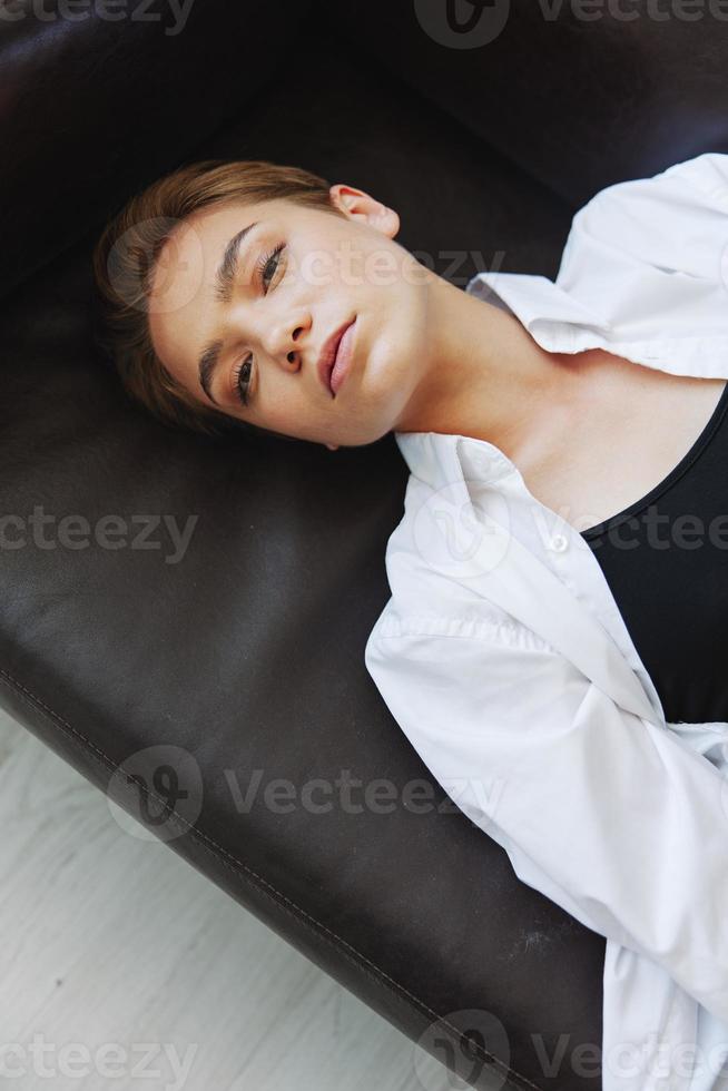 mujer acostado a hogar en el sofá retrato con un corto Corte de pelo en un blanco camisa, sonrisa, depresión en adolescentes, hogar fiesta foto