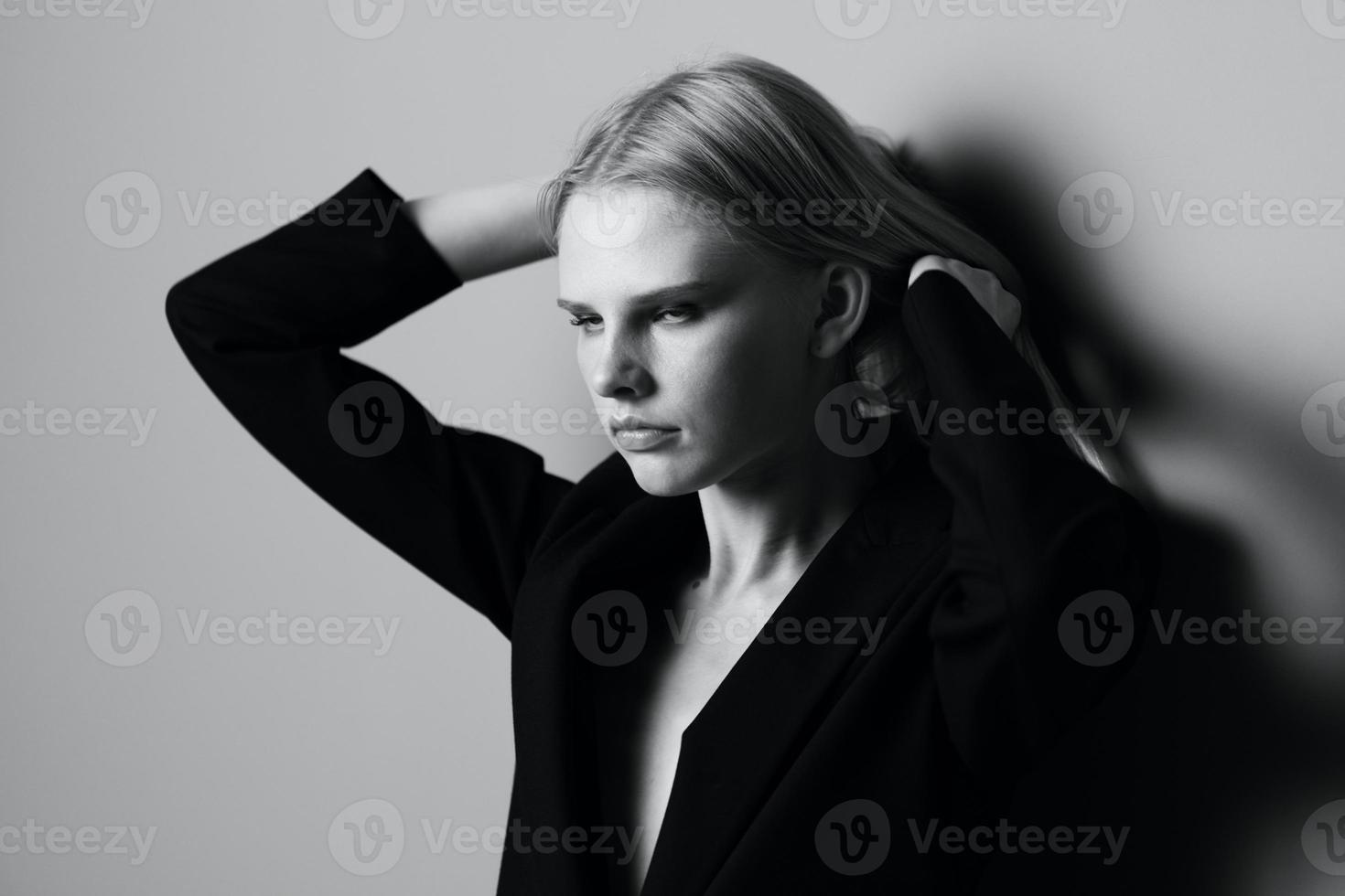 Aesthetic pensive sad blonde young model posing in classic jacket touching stocking hair at studio. Beautiful lady thoughtful looking and caress her curls. Black and White concept photo