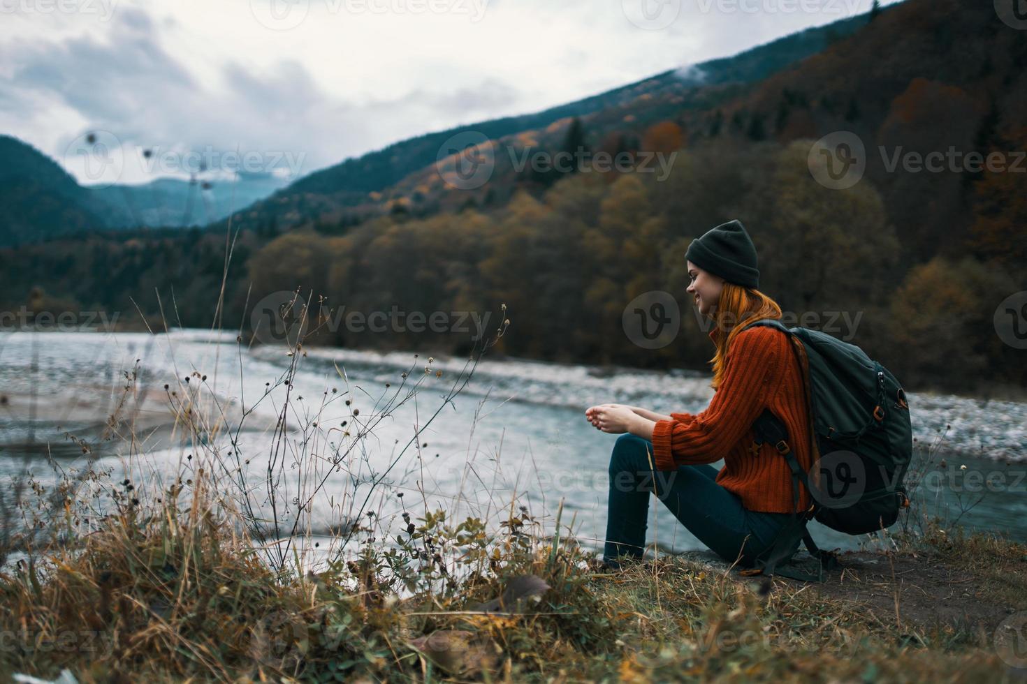 woman near the river in the mountains with a backpack on her shoulders are resting in the autumn forest photo