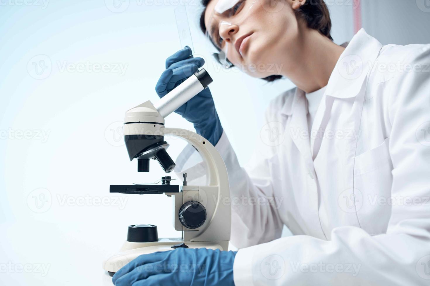 woman scientist in a white coat looking through a microscope study photo