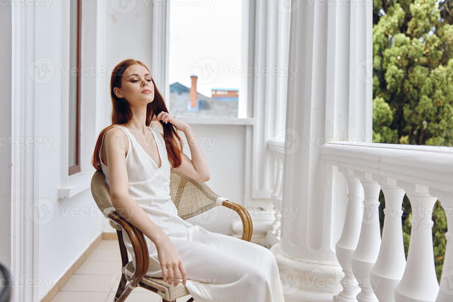 A woman in a white dress sits in a chair on the hotel terrace. photo