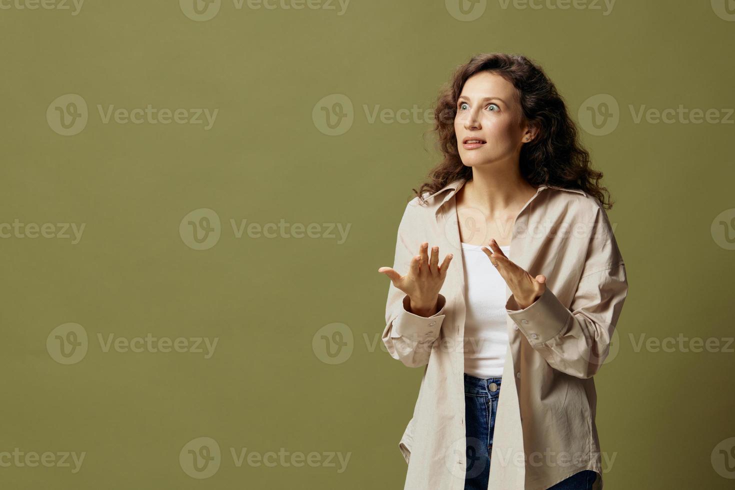 Overjoyed shocked happy curly beautiful female in linen casual shirt gestures while communicating looks aside posing isolated on olive green pastel background. People Lifestyle Emotions. Copy space photo