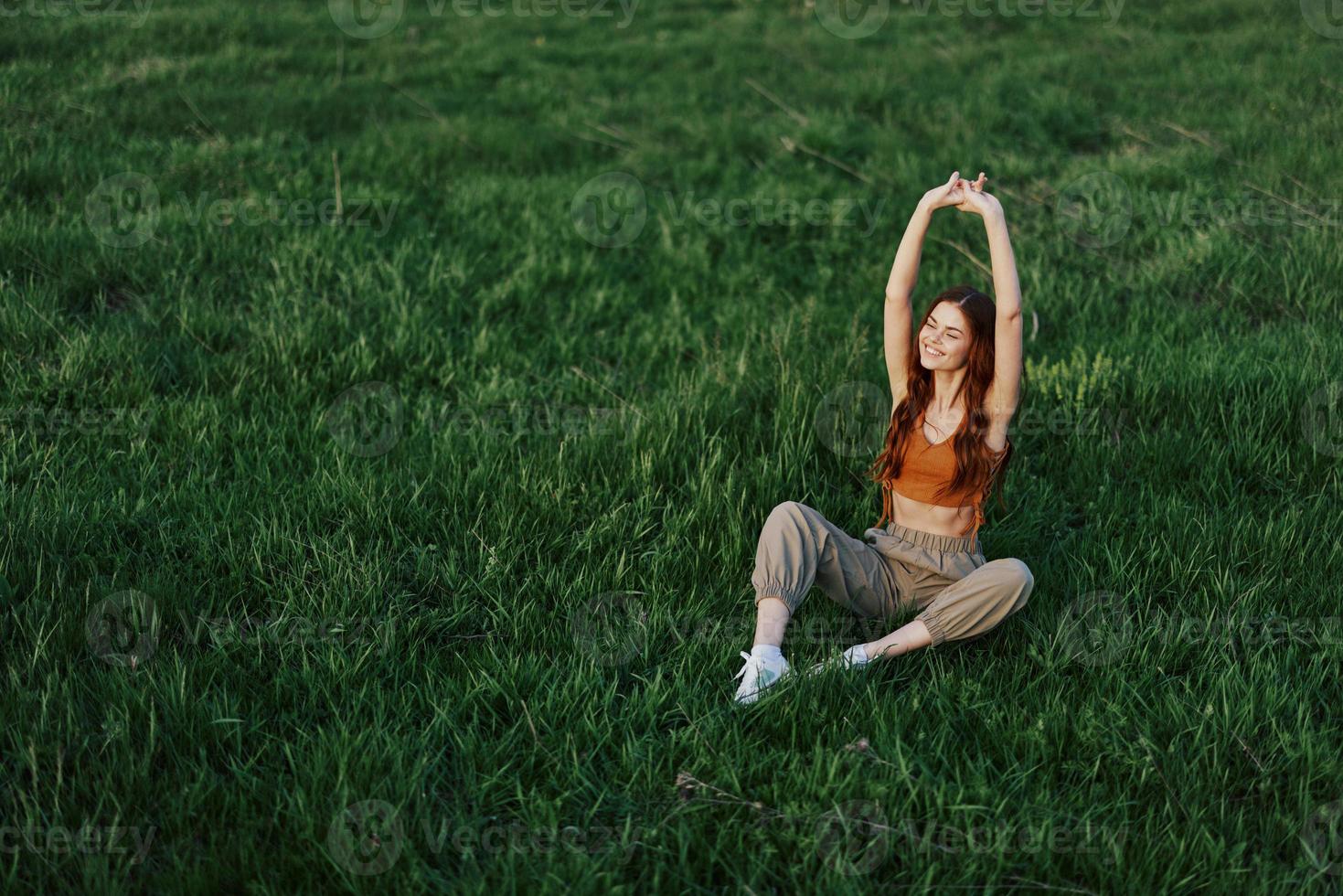 Young sportswoman warming up on the grass in the park on a sunny evening photo