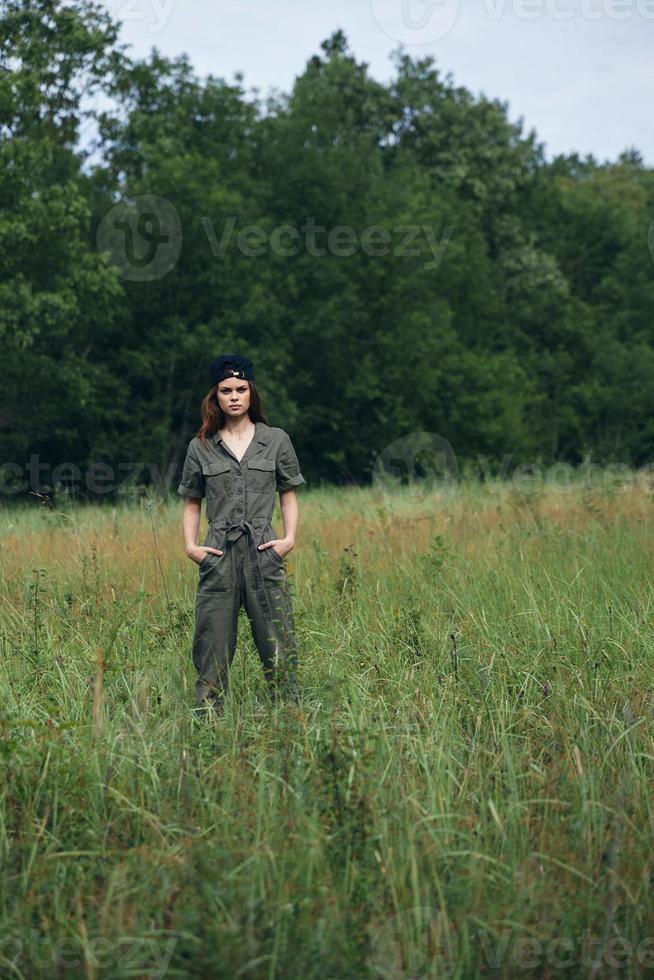 Woman on nature holds his hands in the pockets of green overalls in the meadow photo