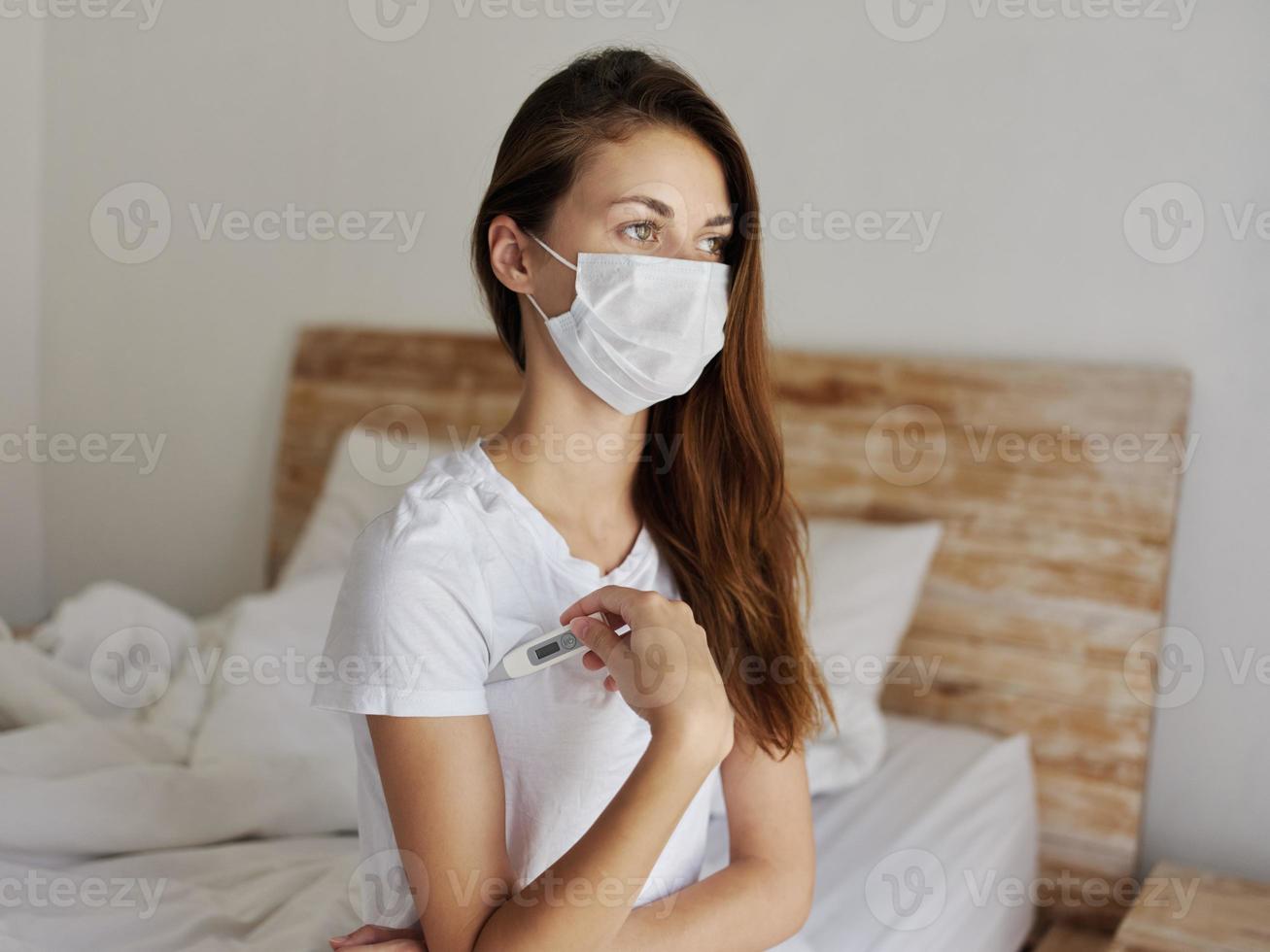 woman with thermometer under her arm wearing medical mask checking