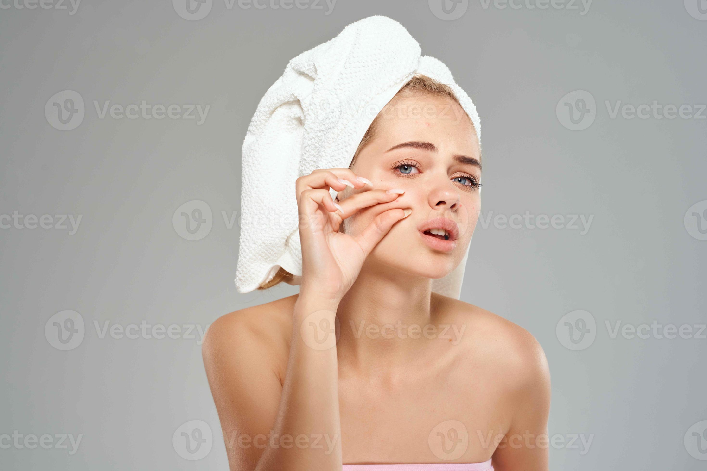 woman with bare shoulders squeeze pimples on her face towel on her head