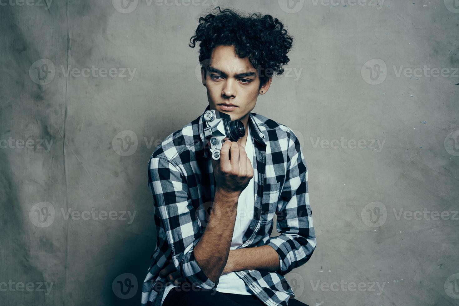 chico en un camiseta y en un tartán camisa examina su pelo en un gris antecedentes recortado ver de cerca foto