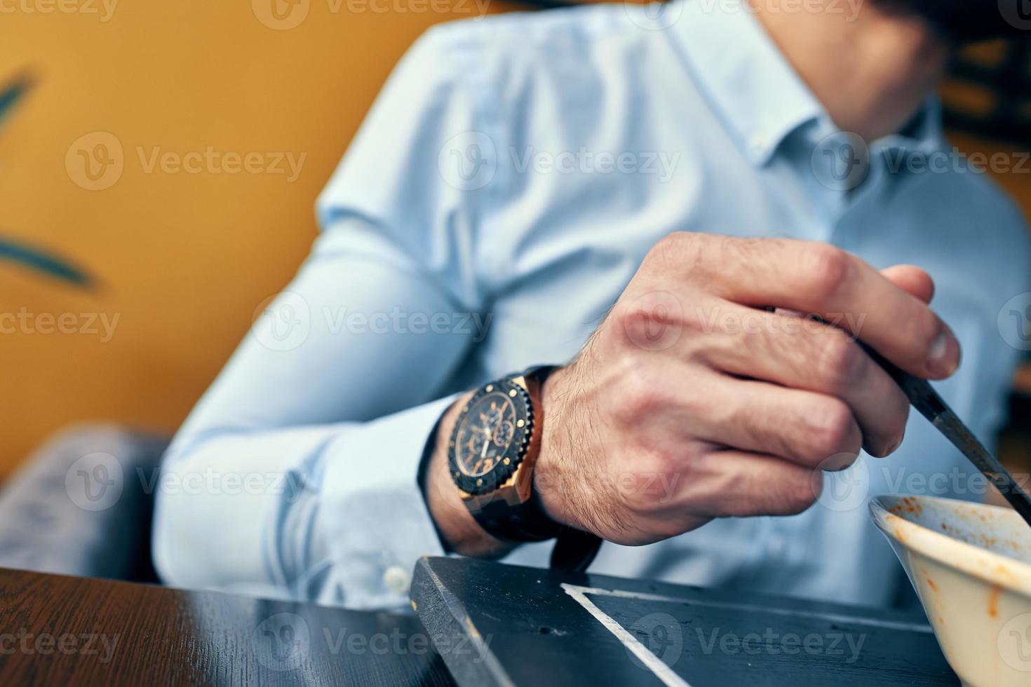 a handsome man with a beard eats borscht in a plate at a table in a cafe and a watch on his hand photo