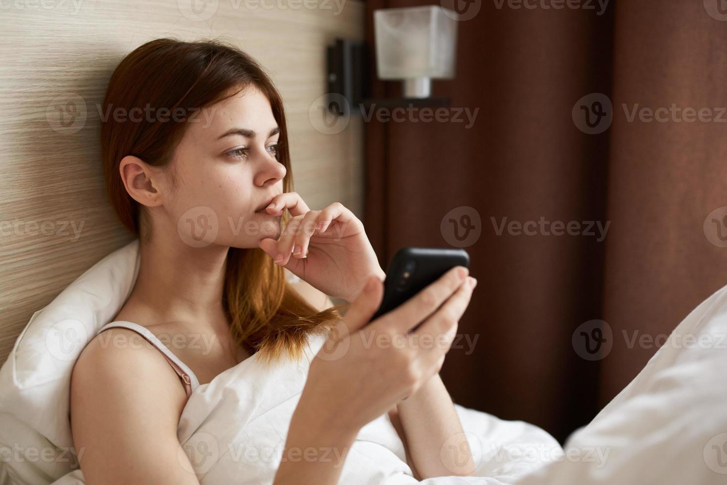 portrait of a woman in bed under a white blanket with a mobile phone and design interior photo