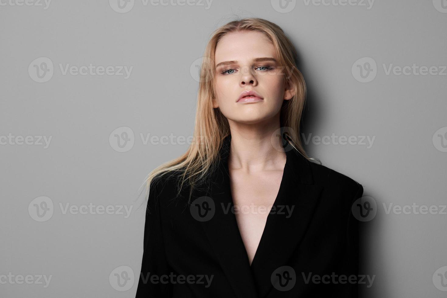 Young expressive beautiful blonde professional model posing isolated in studio dressing in black jacket looks at camera. Fashion Minimalistic concept photo